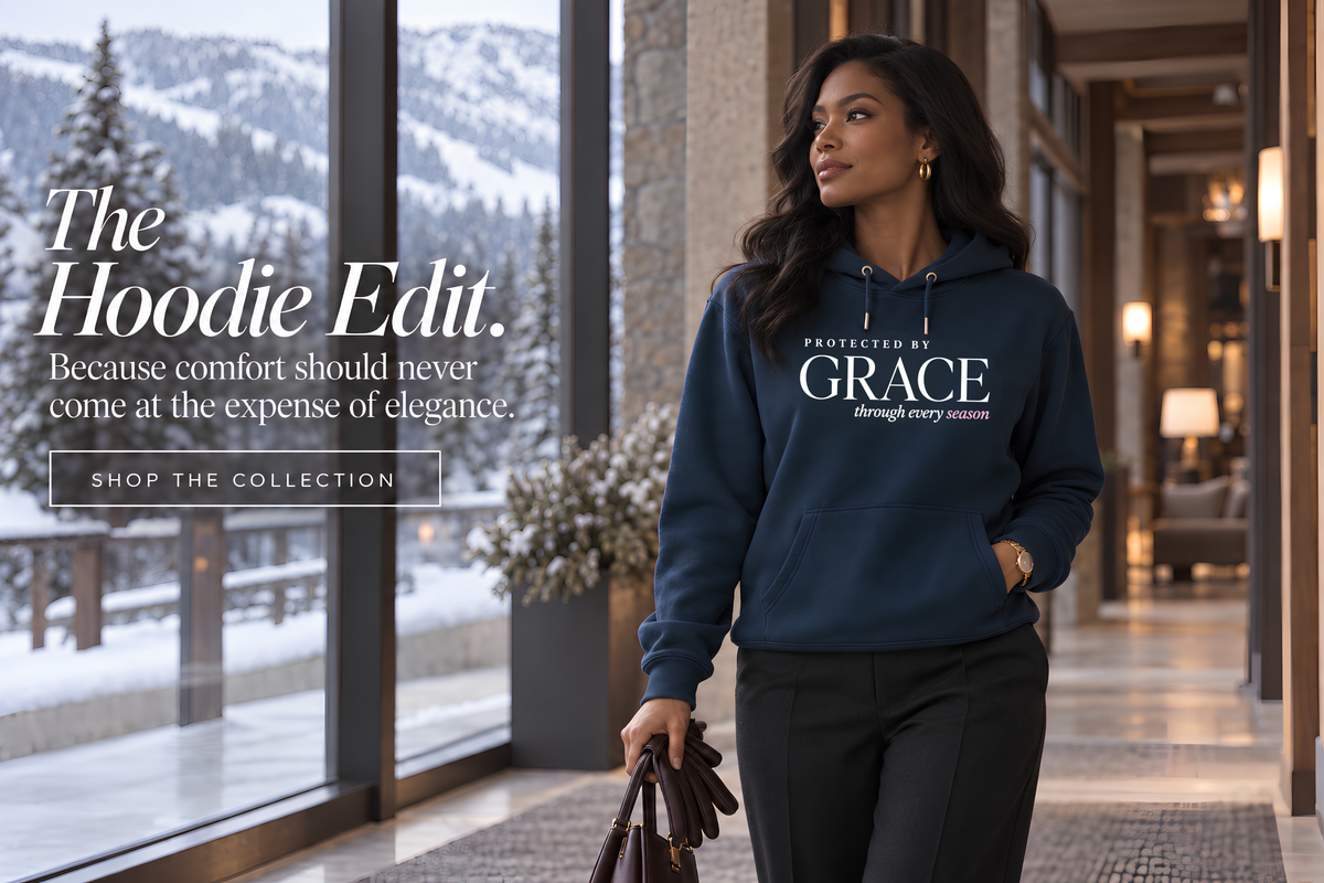 Woman wearing a navy Protected by Grace Christian hoodie with black tailored trousers in a luxury snowy Aspen hotel, styled as an elevated women’s winter outfit.