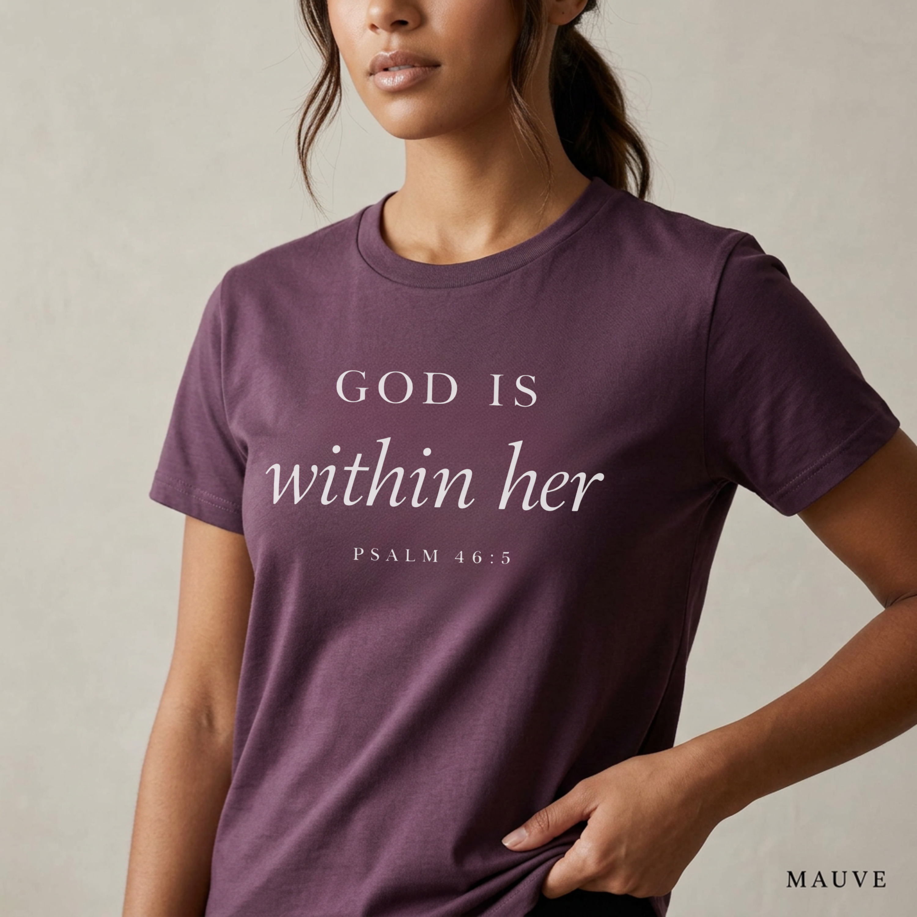 God is within her Psalm 46:5 bible verse on mauve T-shirt. She is standing holding the scripture tee at the hem.