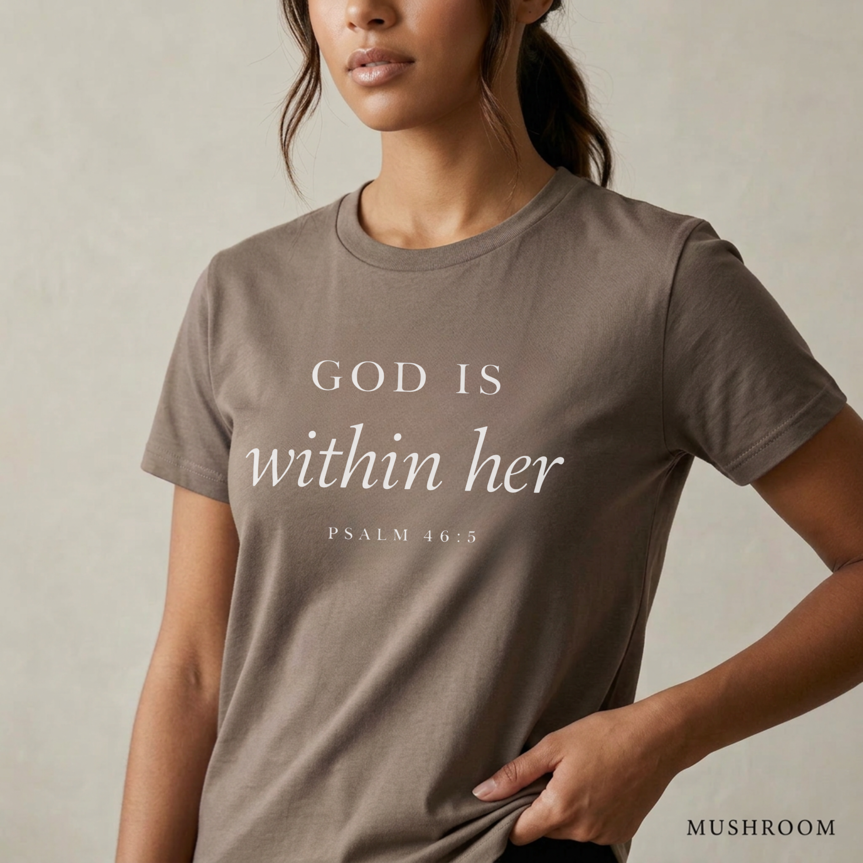 God is within her Psalm 46:5 bible verse on mushroom T-shirt. She is standing holding the scripture tee at the hem.
