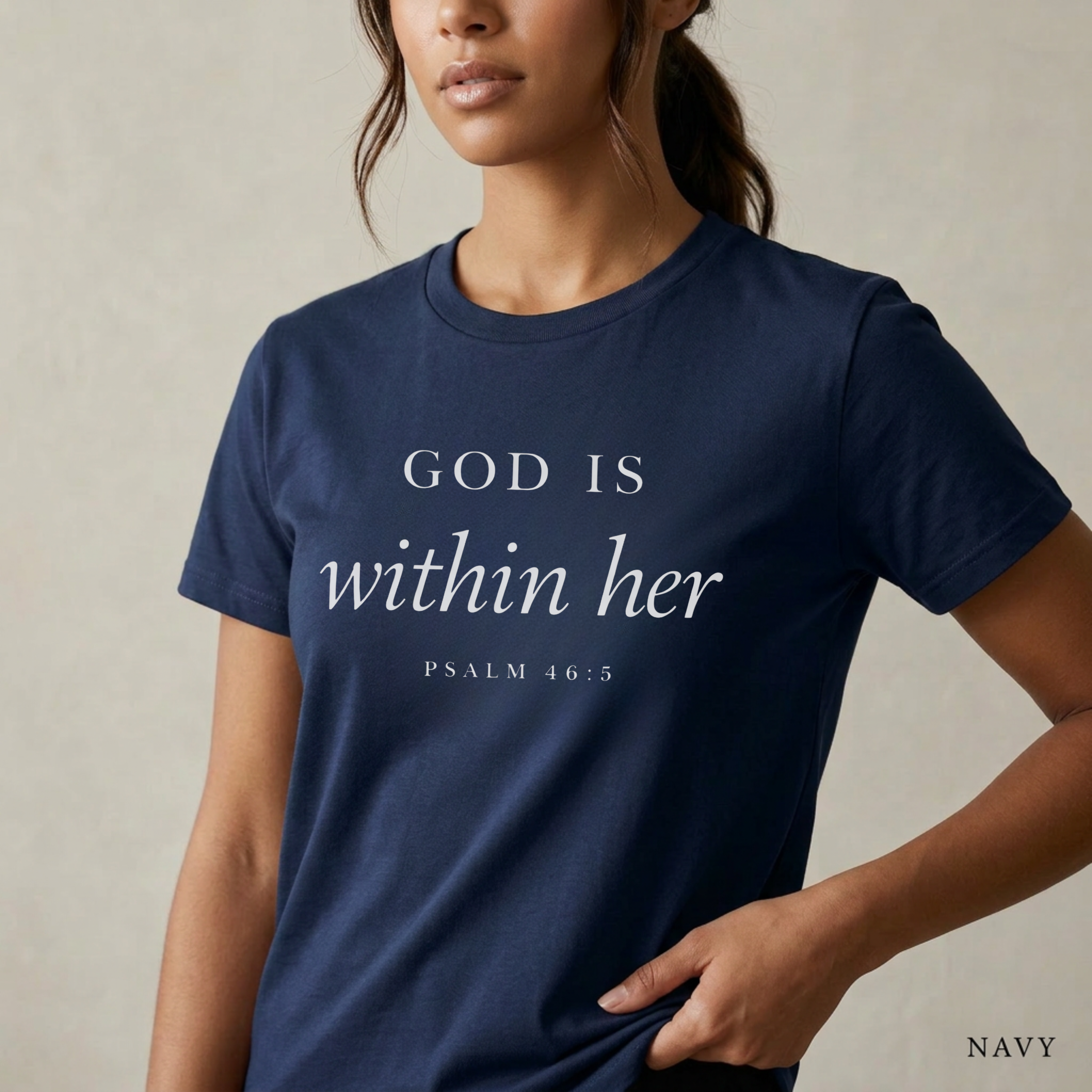 God is within her Psalm 46:5 bible verse on navy T-shirt. She is standing holding the scripture tee at the hem.