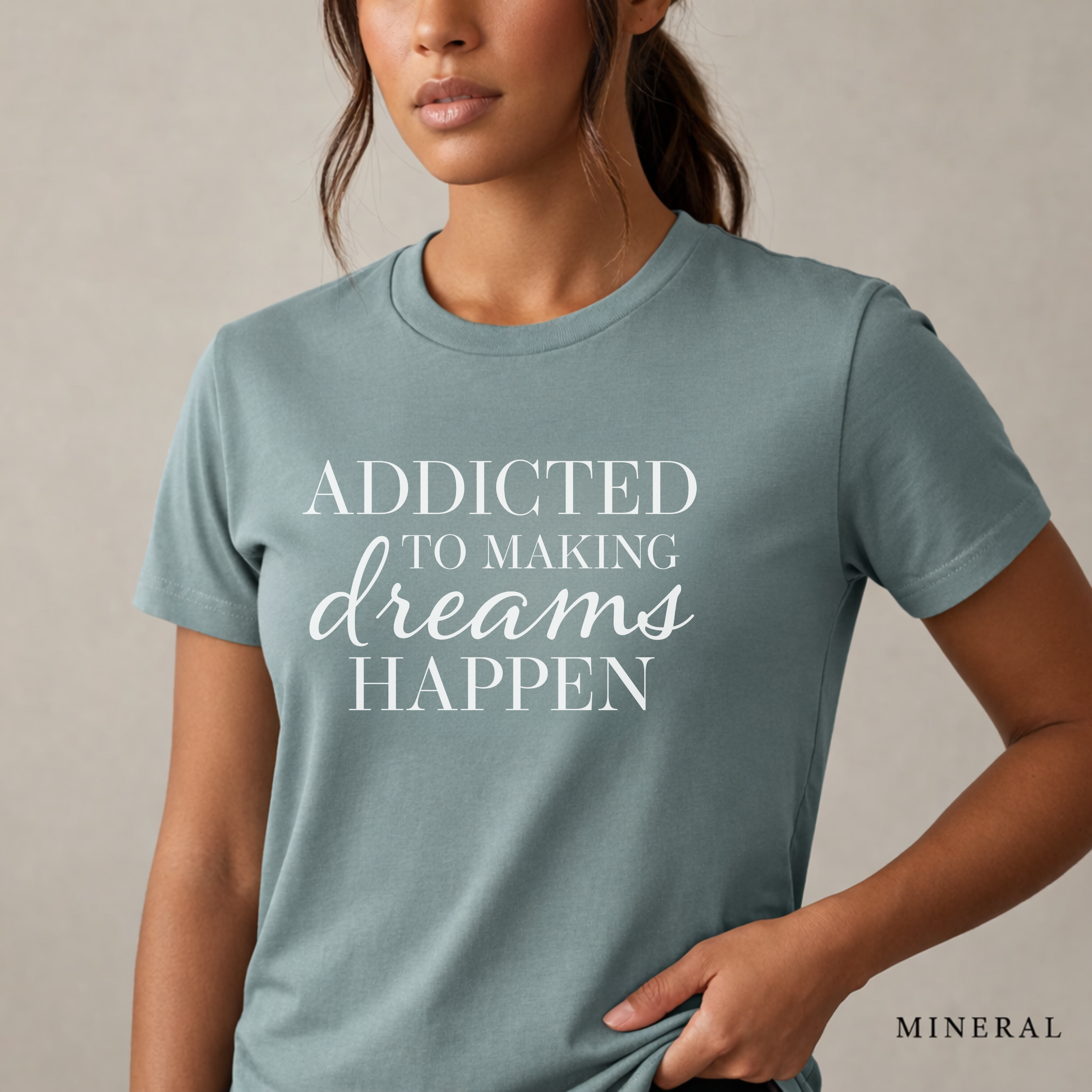 Close-up product photo of a women’s mineral blue graphic tee with elegant white typography, shown on a model in soft natural light with a clean neutral background and refined modern styling.