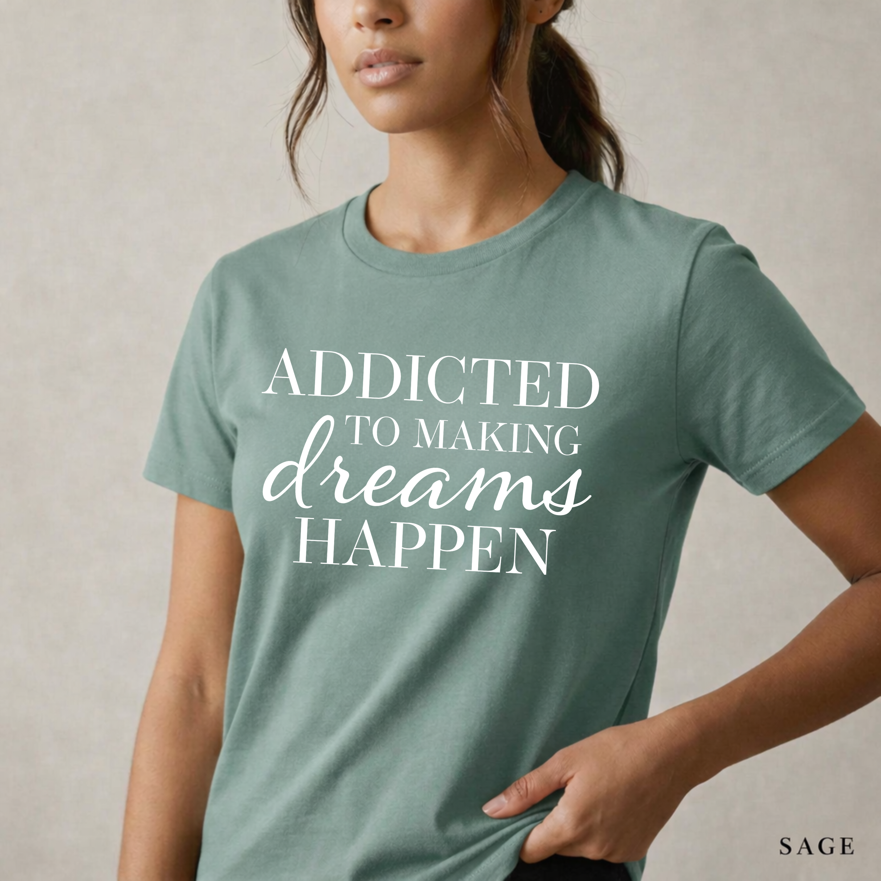 Close-up product photo of a women’s sage green graphic tee with elegant white typography, shown on a model in soft natural light with a clean neutral background and refined modern styling.