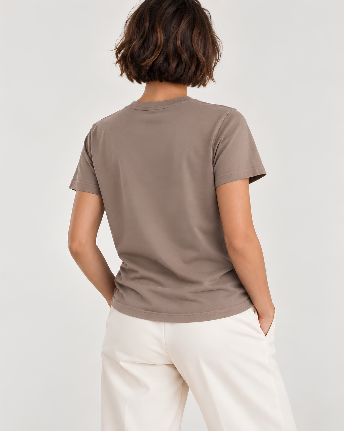 A woman shown from the back wearing a taupe brown short-sleeve crewneck t-shirt and off-white trousers, photographed against a light gray studio background.