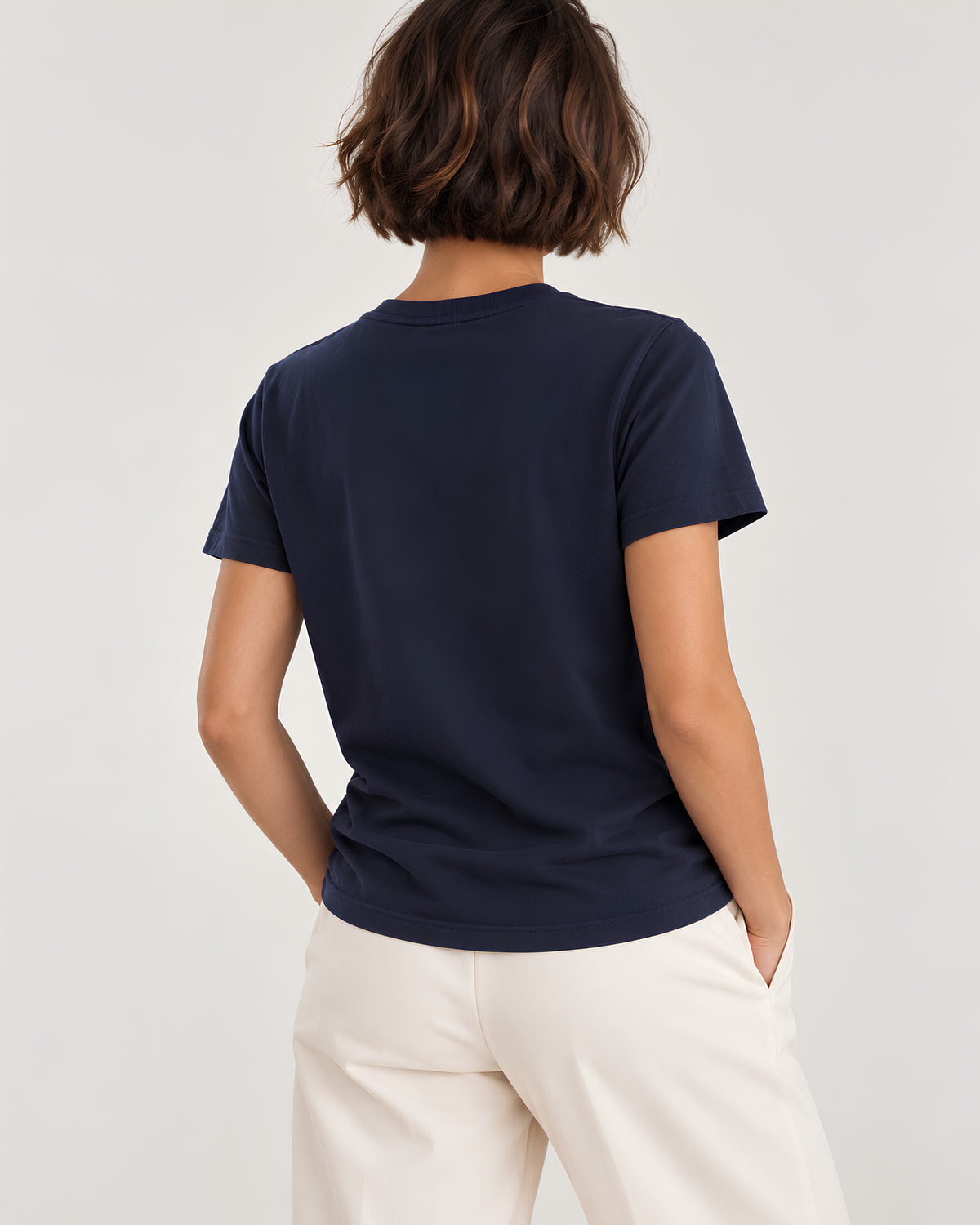 A woman shown from behind wearing a navy blue short-sleeve crewneck t-shirt and off-white trousers, set against a plain light gray studio background.