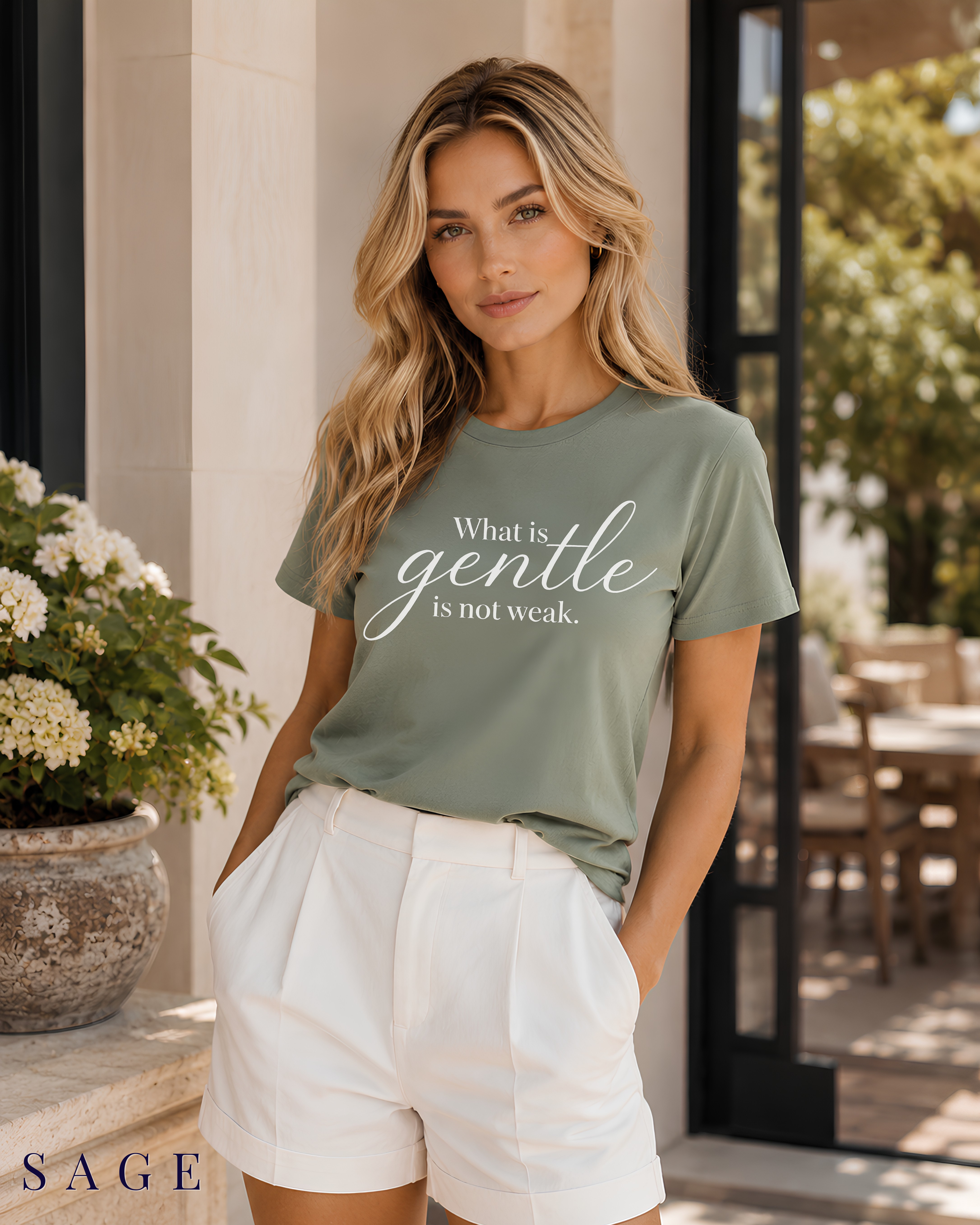 A woman wearing a sage green Christian graphic t-shirt with the text 'What is gentle is not weak.' in white script, paired with white shorts, standing in a sunlit patio setting.