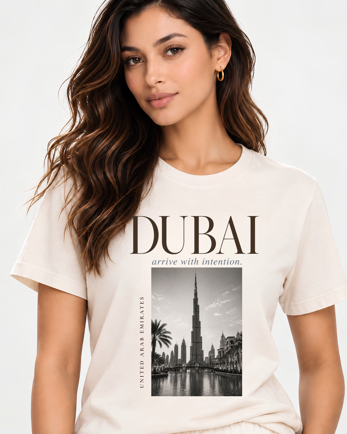 A woman wearing a cream-colored graphic t-shirt with 'DUBAI' and a black-and-white photo of the Burj Khalifa printed on the front, set against a plain light background.