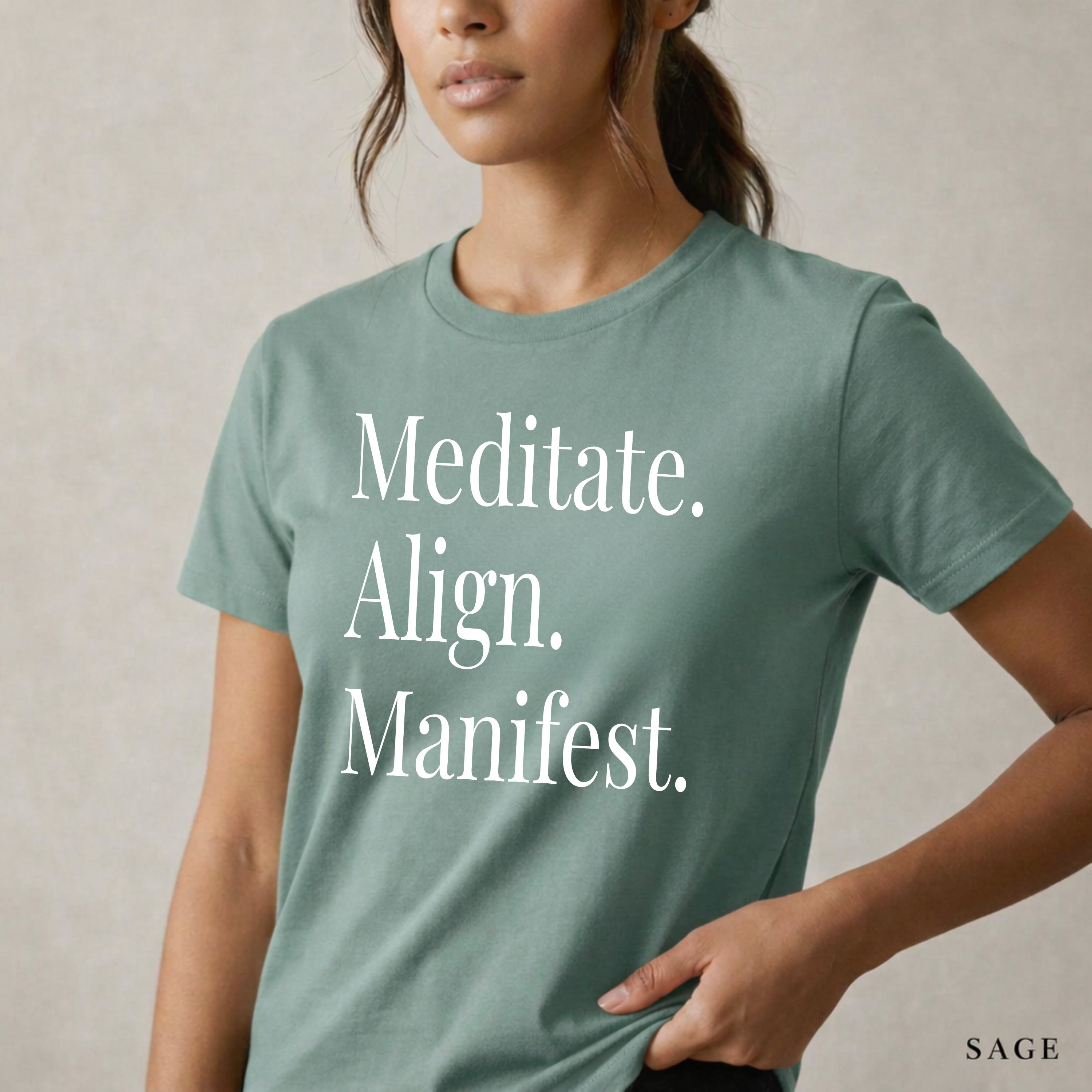 Close-up product photo of a women’s sage green graphic tee with elegant white typography, shown on a model in soft natural light with a clean neutral background and refined modern styling.