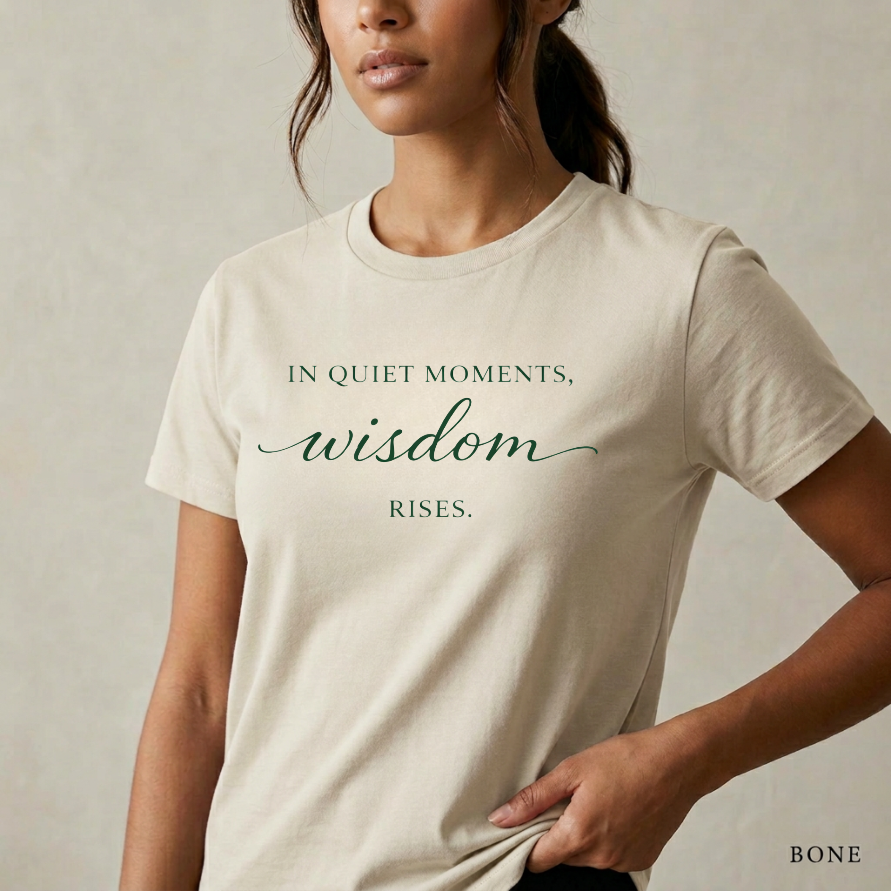 Close-up product photo of a women’s bone graphic tee with elegant white typography, shown on a model in soft natural light with a clean neutral background and refined modern styling.
