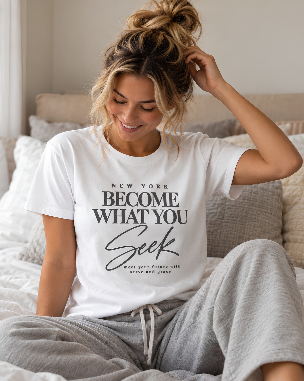 Woman relaxing at home in a New York graphic tee with the “Become What You Seek” message.