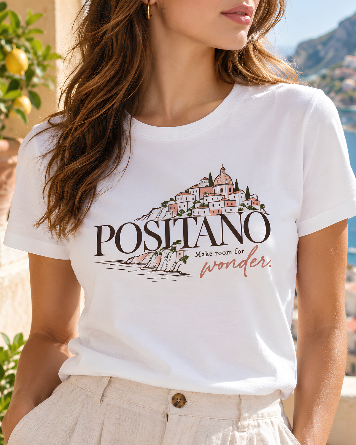 Woman wearing a white Positano graphic tee with a coastal-town illustration and the words “Make room for wonder.”