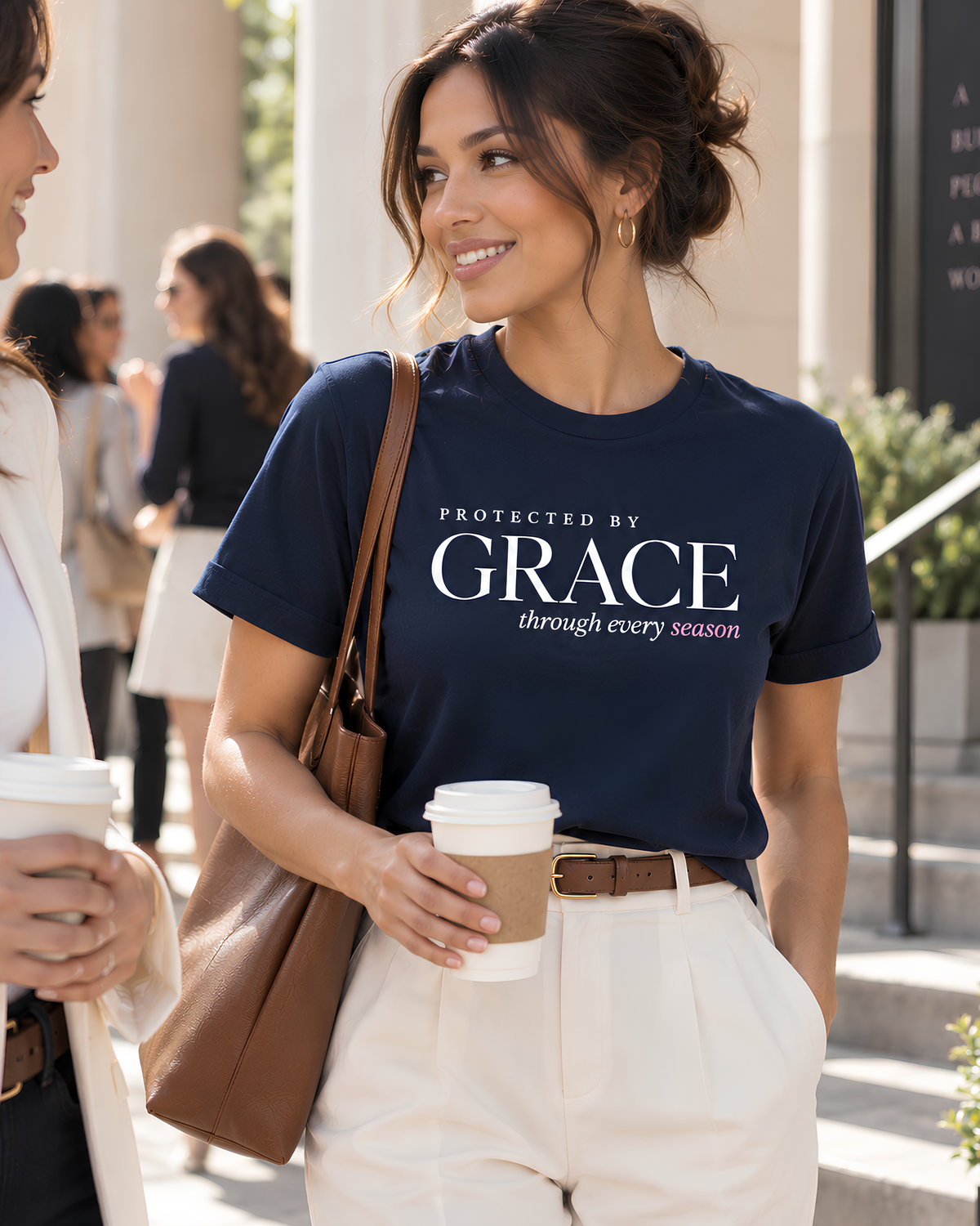 Woman wearing a navy Protected by Grace Christian graphic tee with “through every season” faith message, styled with cream trousers for an elevated everyday look.
