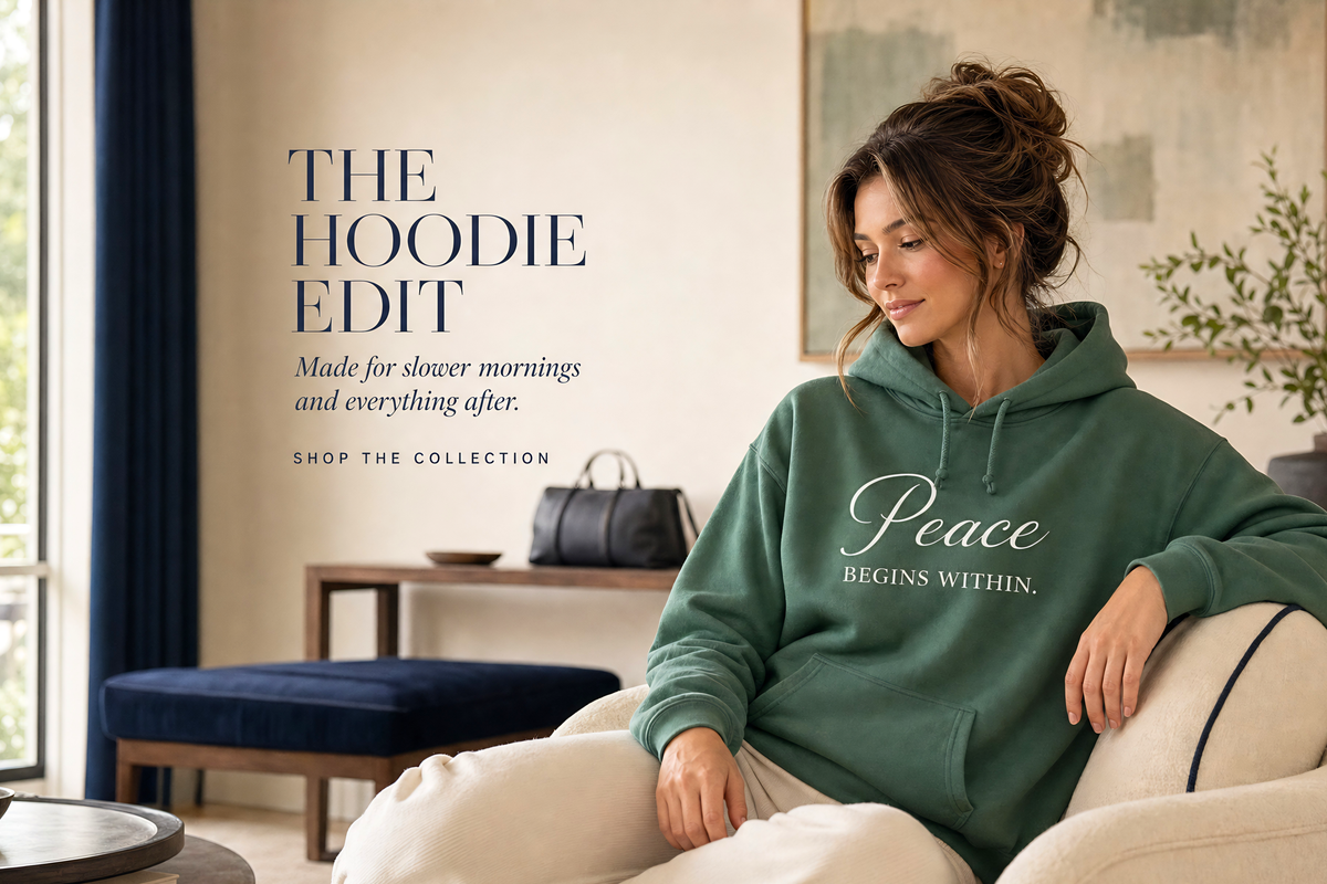 Woman wearing a sage green Peace Begins Within hoodie in a luxury hotel lounge with navy accents, ivory furniture and relaxed editorial styling for Living Redesigned.