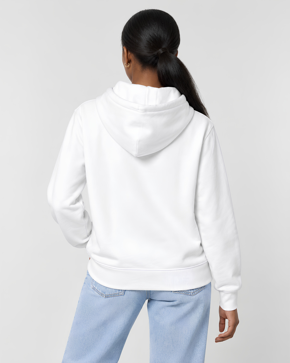 A woman viewed from the back wearing a plain white pullover hoodie and light blue jeans against a light gray studio background.