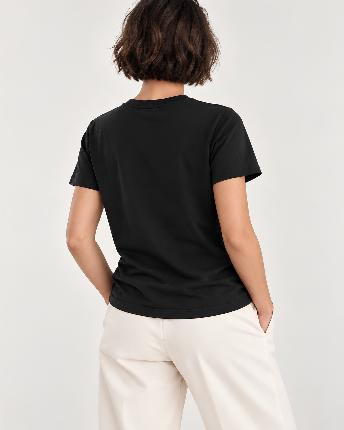 A woman shown from behind wearing a black short-sleeve crewneck t-shirt and off-white trousers, photographed against a clean light gray studio background.