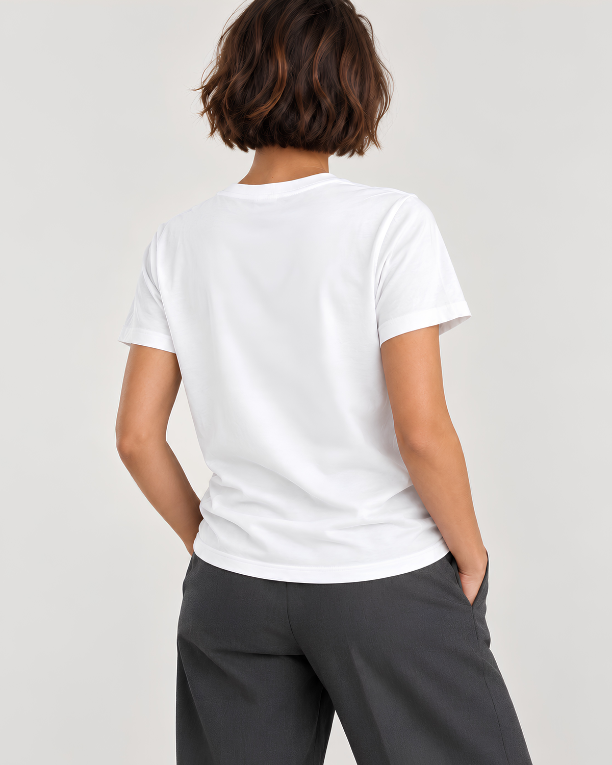A woman shown from the back wearing a plain white short-sleeve crew-neck T-shirt and dark gray trousers, photographed against a light gray studio background.