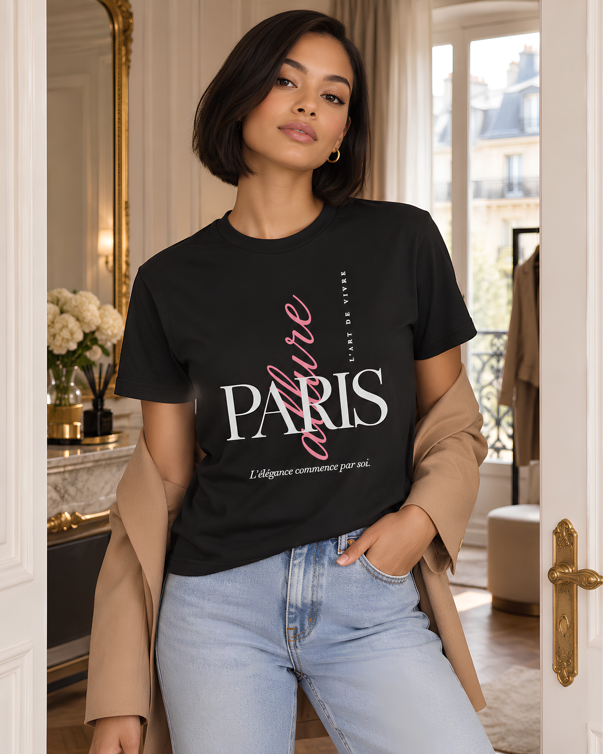A woman wearing a black graphic T-shirt with 'PARIS' and 'affaire' printed on the front, styled with a tan blazer and light blue jeans in an elegant indoor setting.