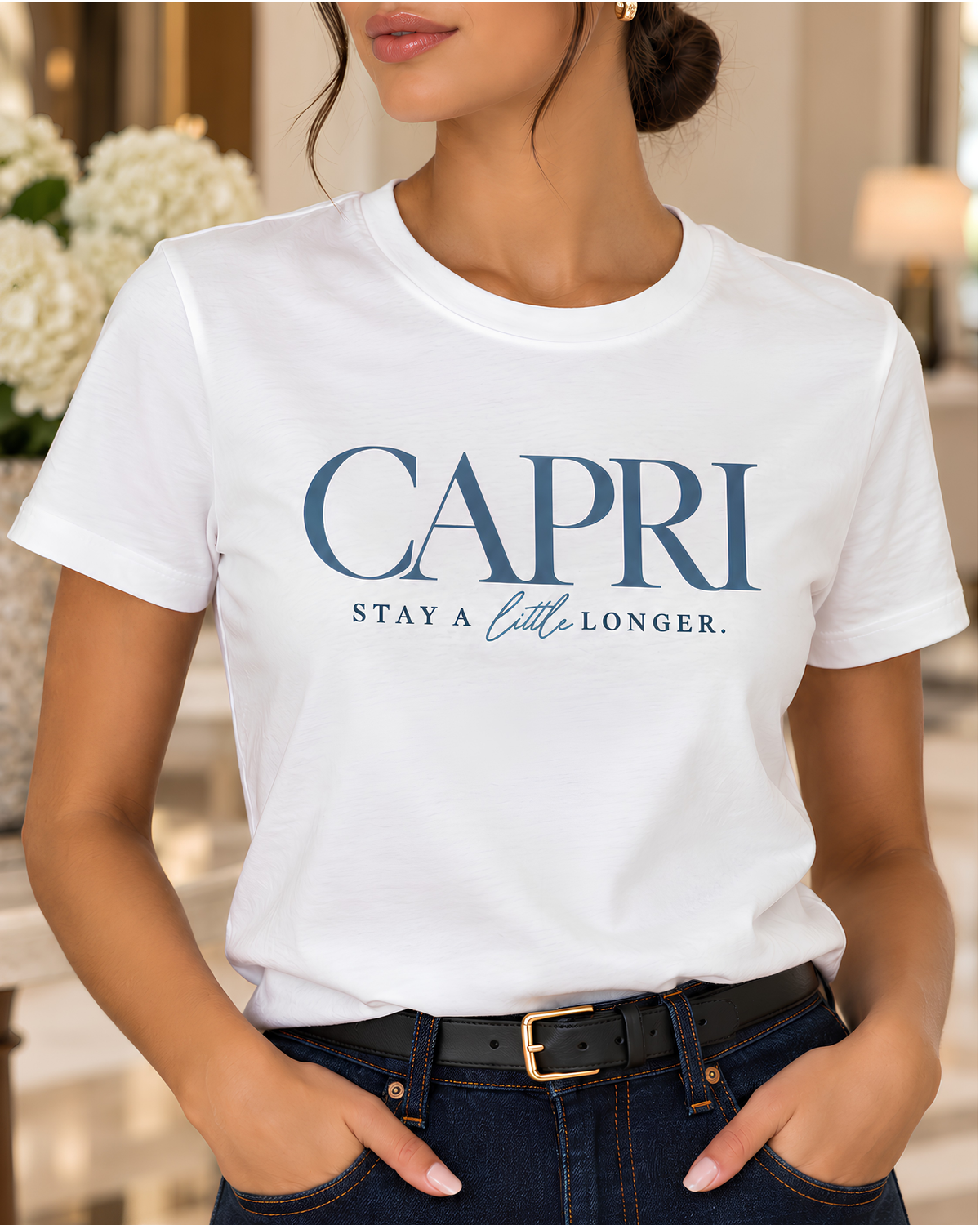 Close-up of woman wearing white Capri Italy graphic tee with Stay a little longer typography, dark indigo jeans and black belt