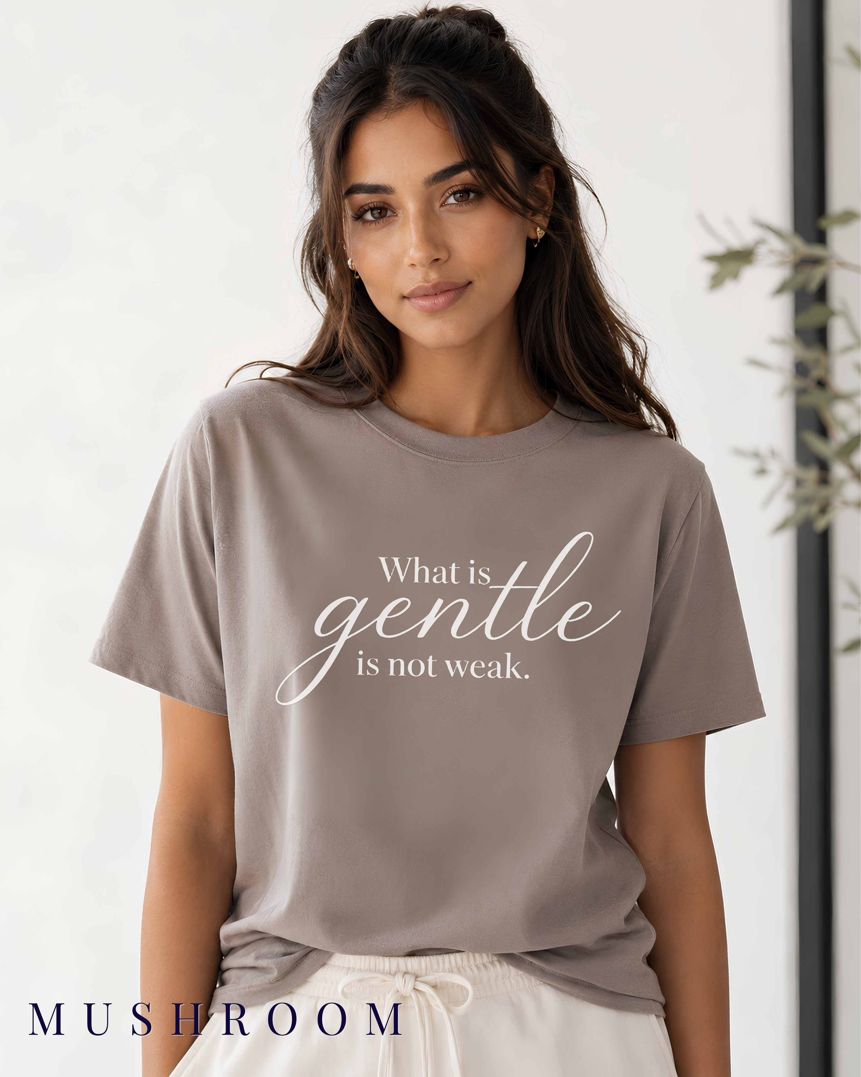 A woman wearing a mushroom tan Christian graphic t-shirt with the white printed text 'What is gentle is not weak.' She is also wearing white drawstring pants.