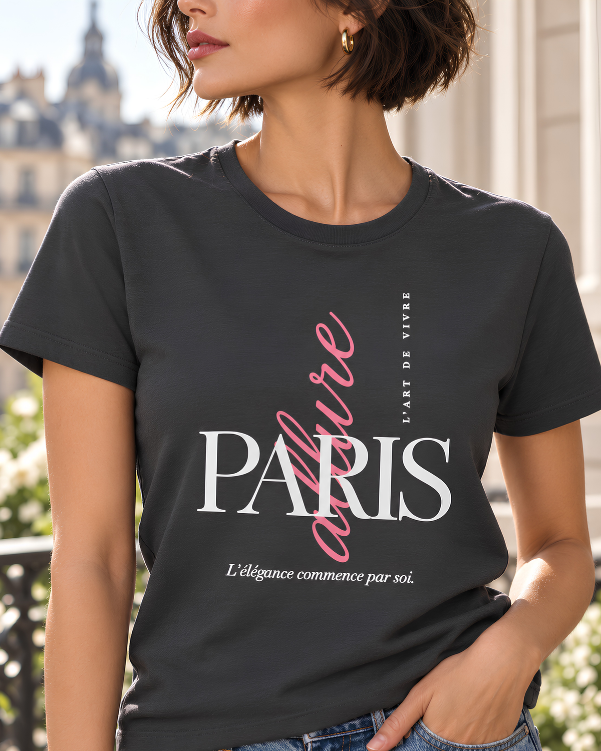 A woman wearing a dark charcoal gray graphic T-shirt with 'PARIS' in white and 'L'Esprit Vivre' in pink script, paired with light blue jeans against a plain light gray background.