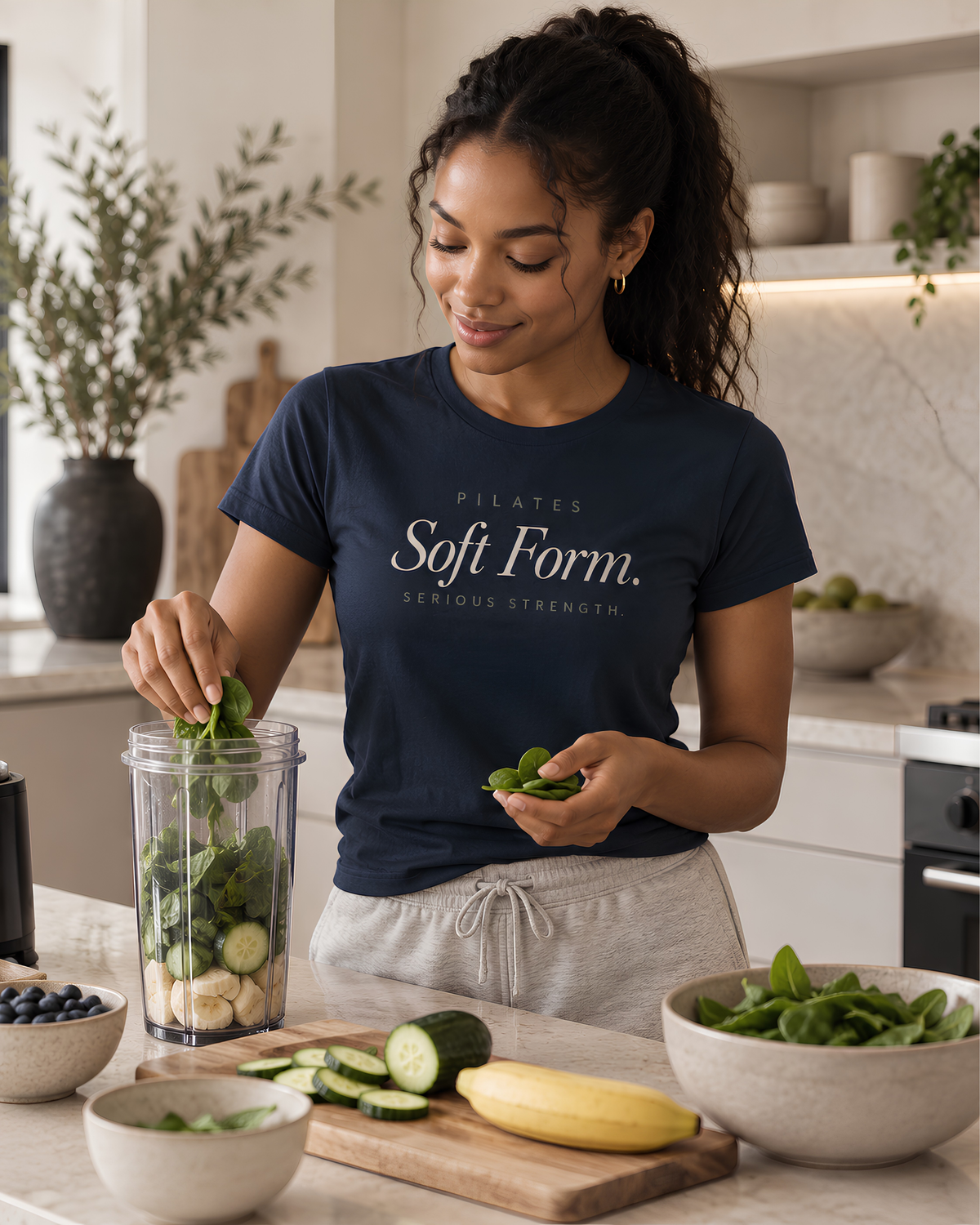 Woman with curly dark hair wearing a black Pilates graphic T-shirt with “Soft Form. Serious Strength.” lettering in a gym.