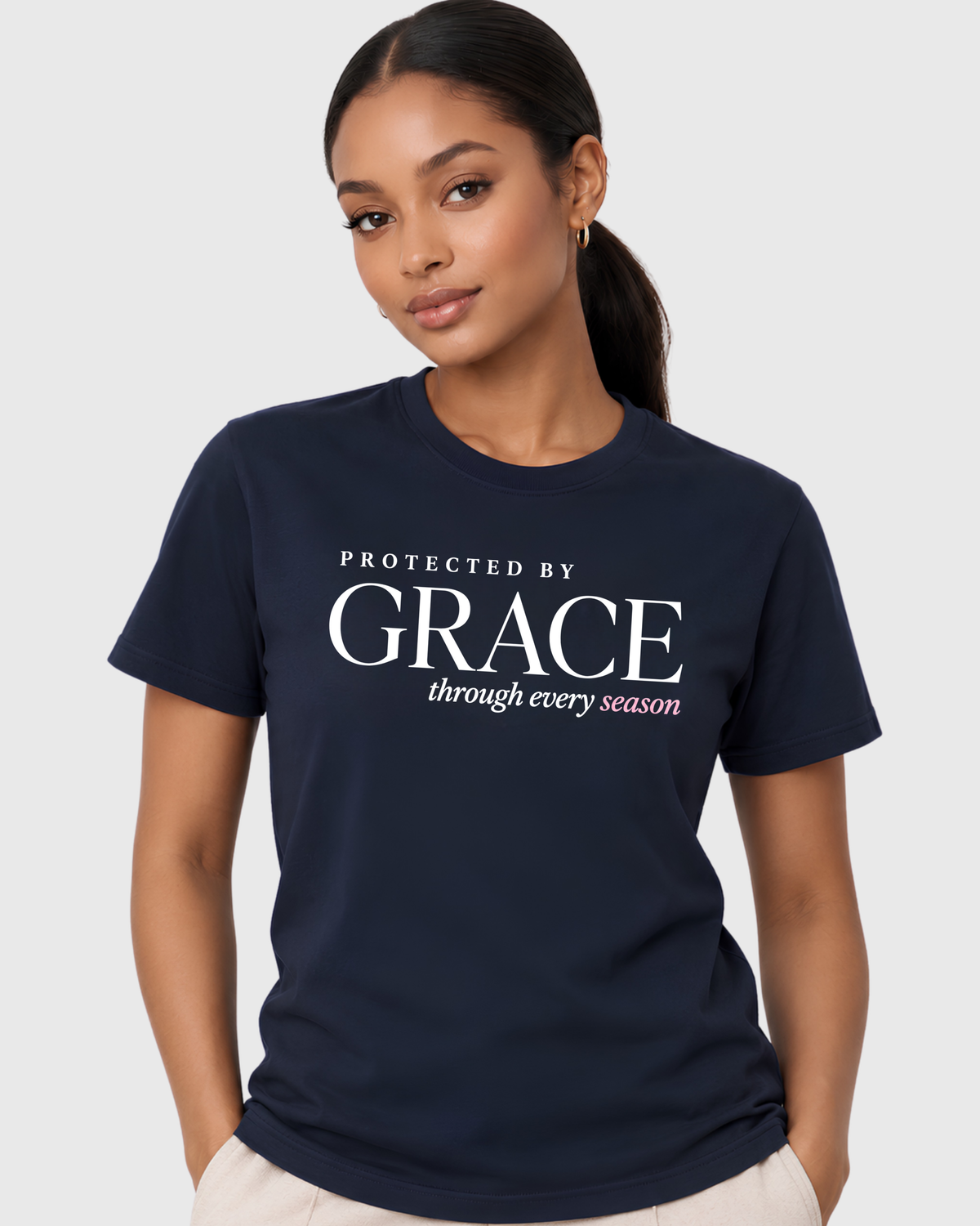 Women’s Christian graphic tee in navy featuring “Protected by Grace through every season,” styled with ivory trousers for a refined inspirational faith shirt look.