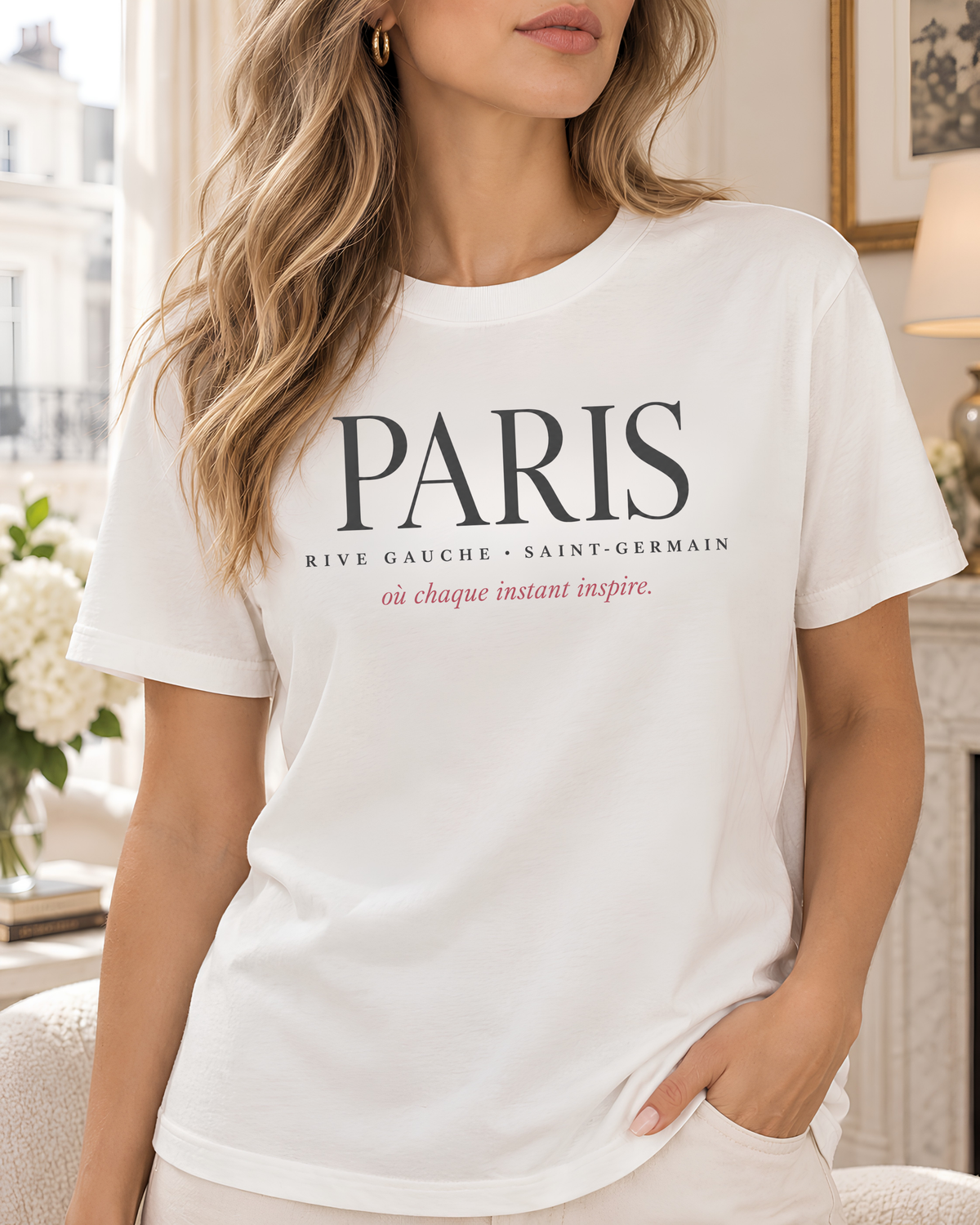 A woman wearing a white short-sleeve crewneck T-shirt with 'PARIS' printed in black across the chest, along with smaller black and pink text below, against a clean white background.