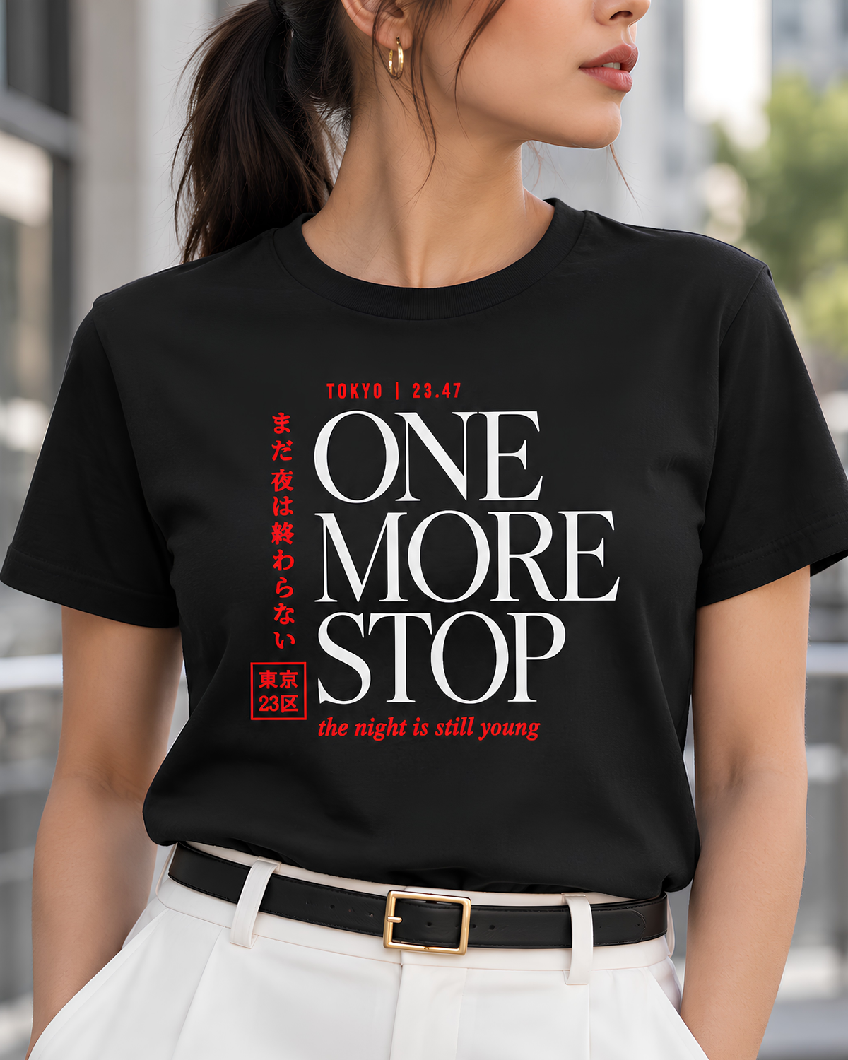 A woman wearing a black short-sleeve graphic T-shirt with bold white and red text reading 'ONE MORE STOP' and smaller Japanese text, photographed against a light gray studio background.