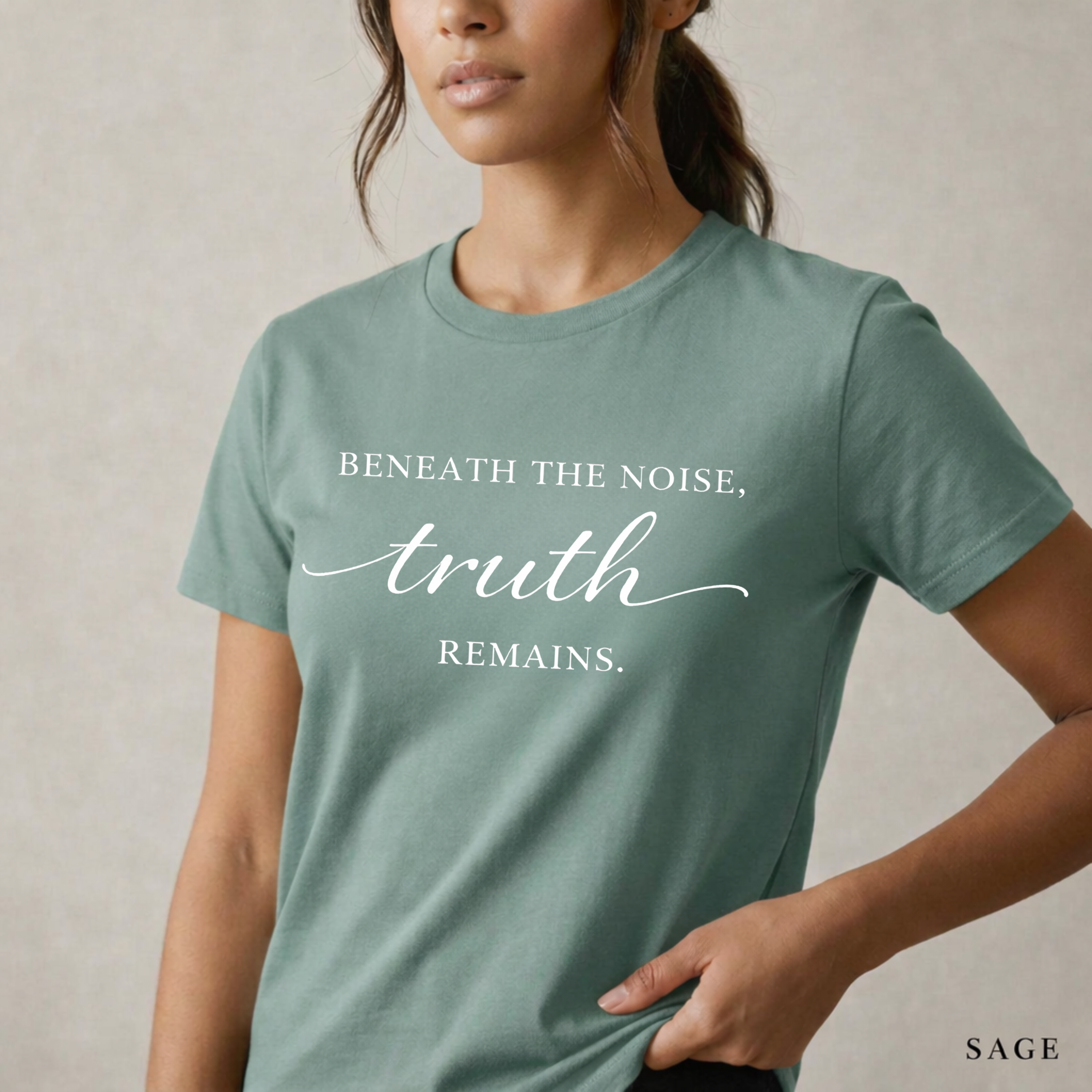 Close-up product photo of a women’s sage green graphic tee with elegant white typography, shown on a model in soft natural light with a clean neutral background and refined modern styling.