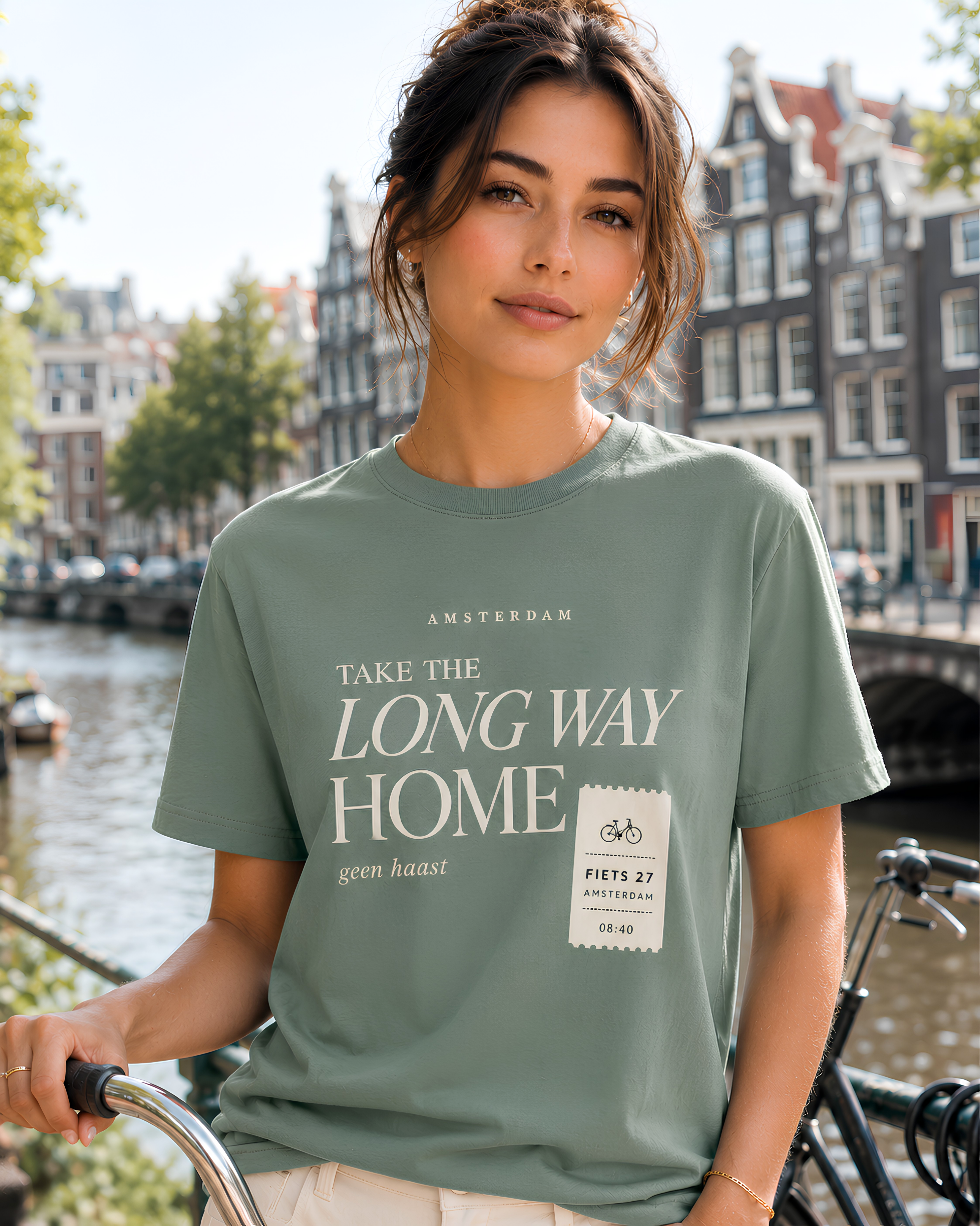Woman wearing sage Amsterdam travel T-shirt with Take the Long Way Home and geen haast design beside an Amsterdam canal