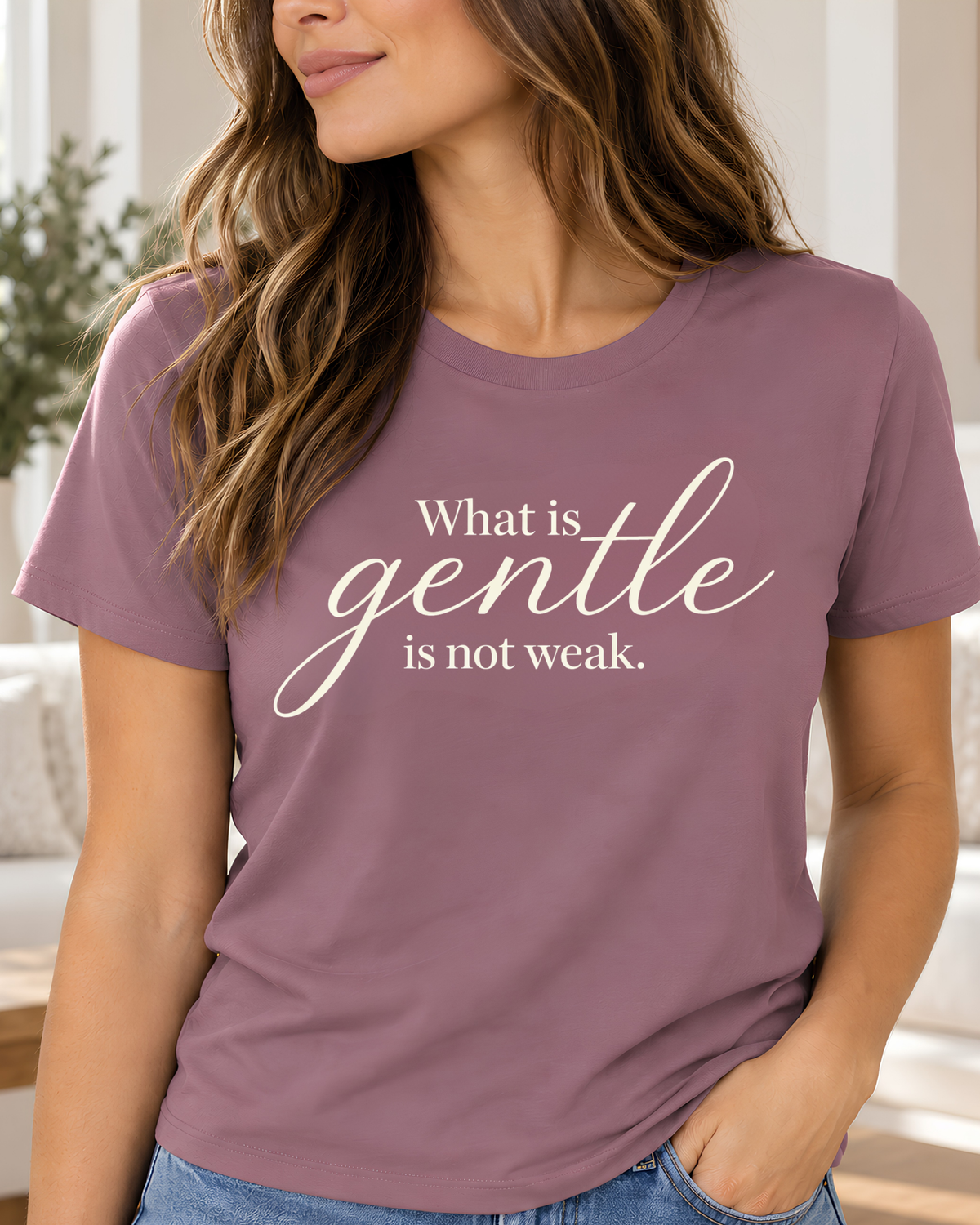 A woman wearing a short-sleeve crewneck t-shirt in a deep plum purple color, featuring the white printed text 'What is gentle is not weak.' on the front, paired with white pants against a clean white background.