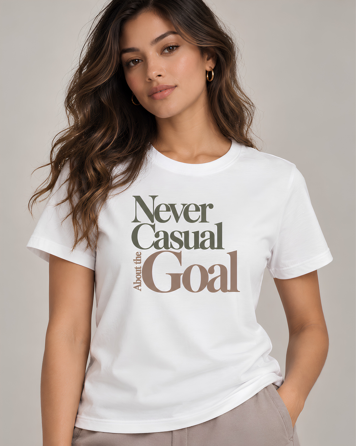 White motivational T-shirt for women featuring “Never Casual About the Goal” in muted olive and warm taupe editorial typography.
