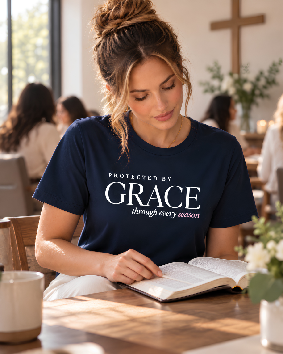 Woman wearing a navy “Protected by Grace through every season” Christian graphic tee while reading the Bible at a women’s church Bible study.