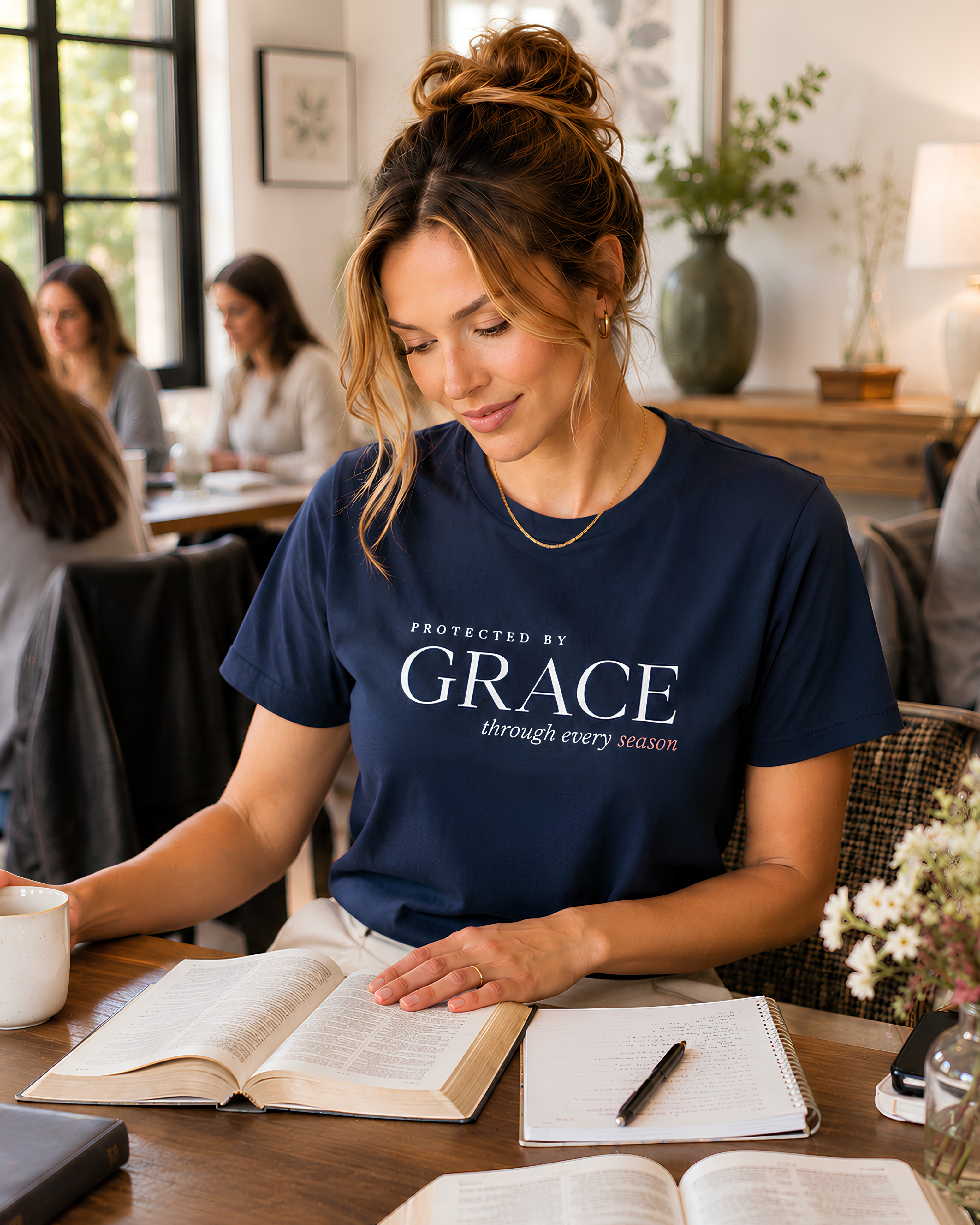 Woman wearing a navy Protected by Grace Christian T-shirt for women while reading the Bible at a women’s Bible study.