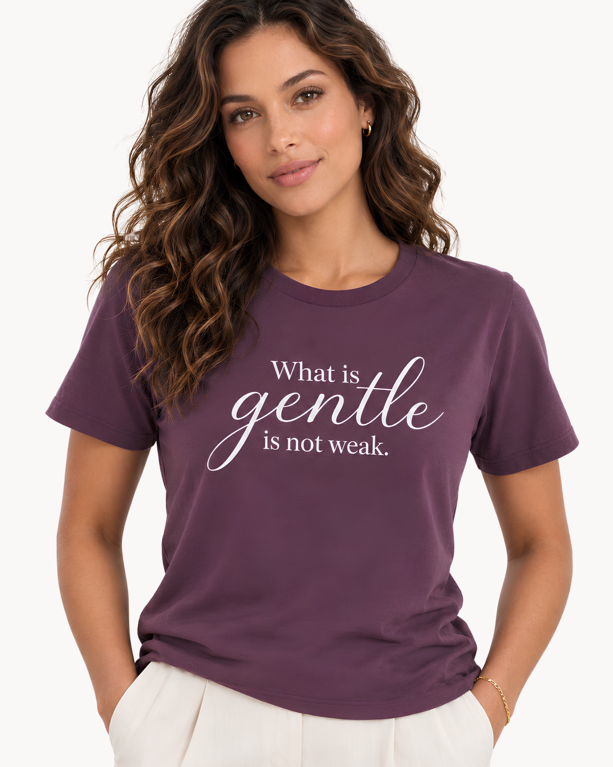 A woman wearing a short-sleeve crewneck t-shirt in a deep plum purple color, featuring the white printed text 'What is gentle is not weak.' on the front, paired with white pants against a clean white background.
