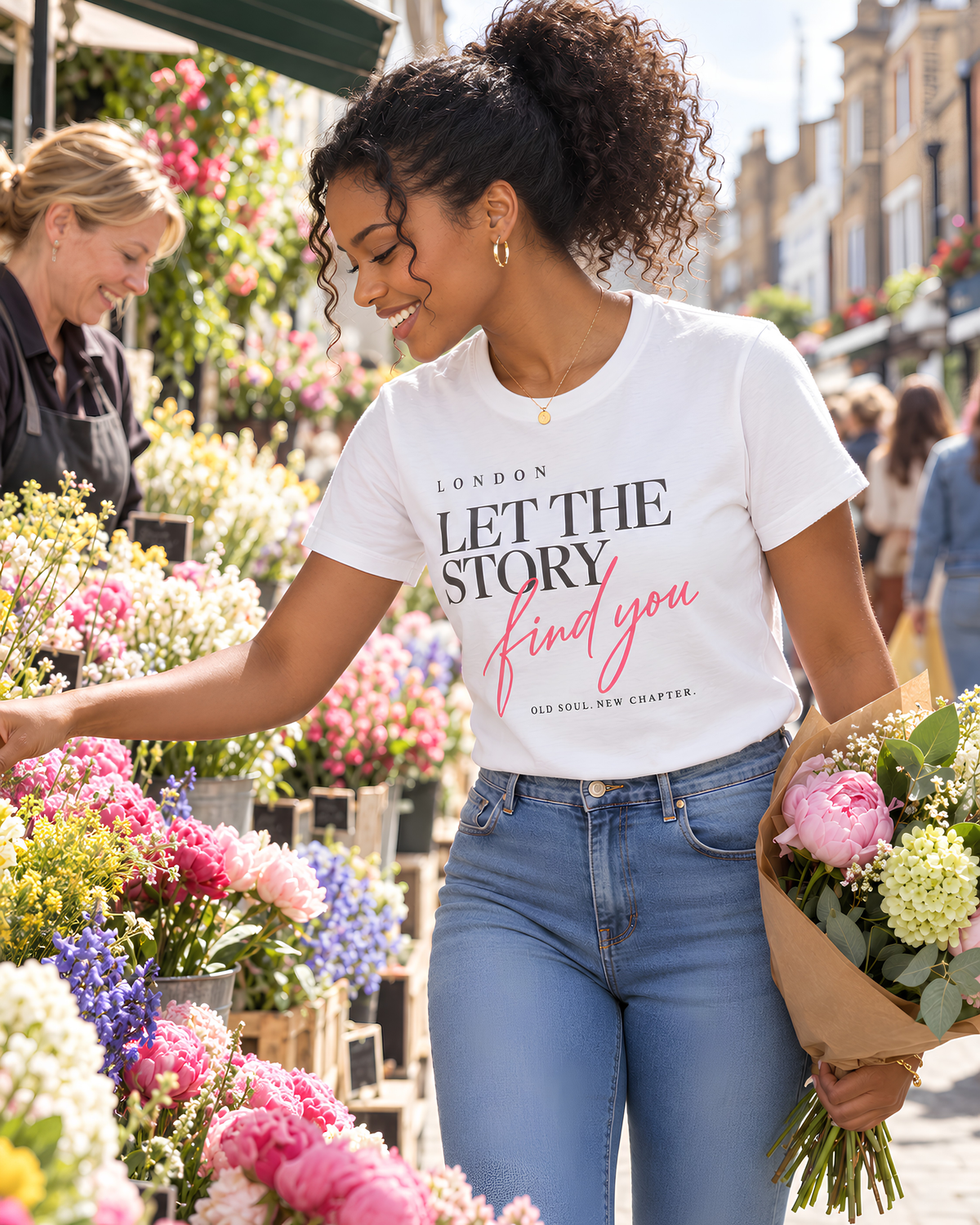 Woman wearing a white London “Let the Story Find You” graphic tee while choosing flowers at Columbia Road Flower Market in London.