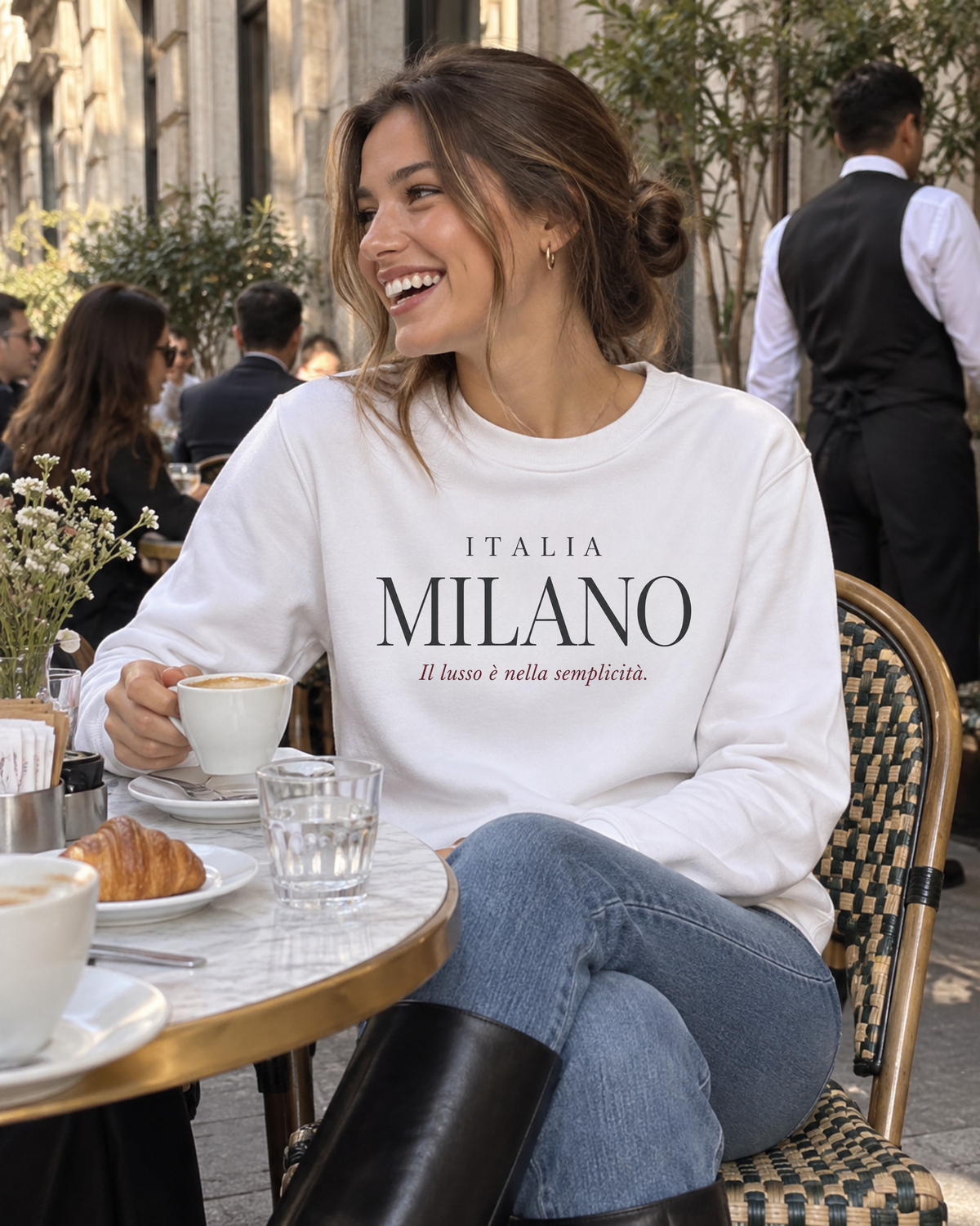 Young woman wearing a white Milano Italy travel sweatshirt with jeans and black leather boots while having coffee at an upscale Milan café.